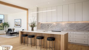 A modern kitchen with a marble countertop, wooden bar stools, and white cabinets. - Downtown Traverse City Penthouse w/ Private Rooftop (Traverse City)