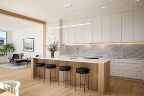 A modern kitchen with a marble countertop, wooden bar stools, and white cabinets. - Downtown Traverse City Penthouse w/ Private Rooftop (Traverse City)