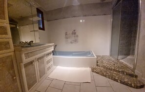 Un baño con bañera, ducha, tocador con espejo y suelo de baldosas.