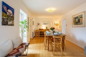 Un coin repas avec une table en bois dressée pour six personnes, un canapé, une plante et des œuvres d’art accrochées aux murs.