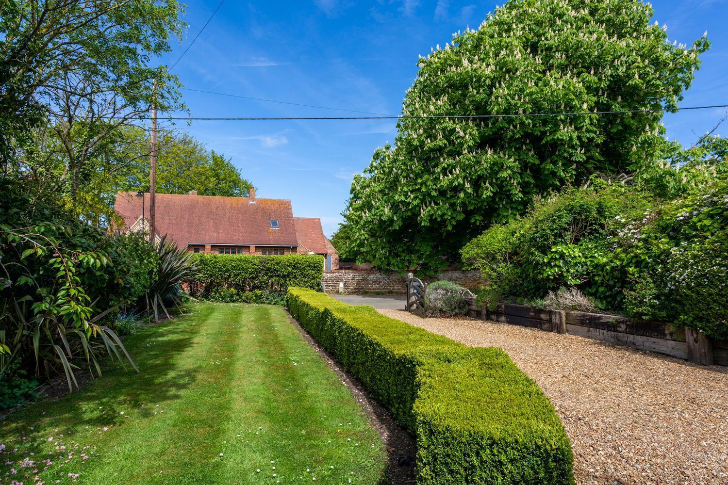A well-maintained garden with a lawn, hedges, and a brick building.