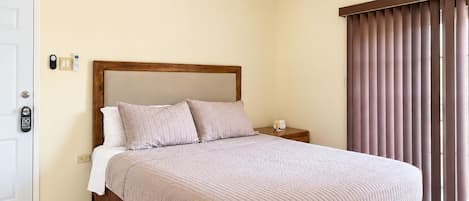 Comfortable Queen bed with soft bedding, ceiling fan, bedside table, and sliding glass doors with privacy blinds studio 1.