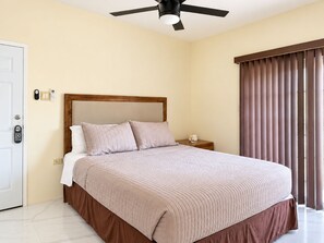 A hotel room with a bed, a nightstand, a ceiling fan, a door, and a window with curtains. - The Vista Inn Studio #1 (Falmouth)