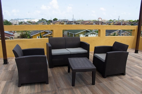 A balcony with wicker furniture, a yellow wall, and a view of residential buildings.. The Vista Inn Studio #1