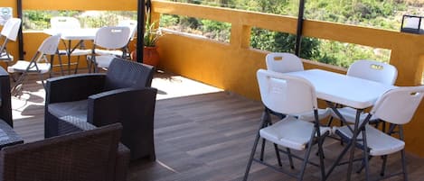 An outdoor patio with wicker furniture and white plastic chairs, overlooking a green landscape.