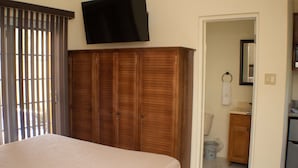Een slaapkamer met een bed, een kledingkast, een televisie en een badkamer die door een open deur zichtbaar is.