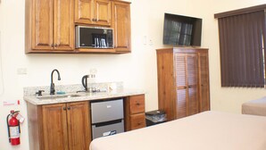 A compact kitchen with wooden cabinets, a microwave, a sink, and a small refrigerator. - The Vista Inn Studio #2 (Falmouth)