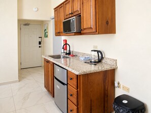 A compact kitchen with wooden cabinets, a stainless steel refrigerator, a microwave, a coffee maker, and a trash bin. - The Vista Inn Studio #2 (Falmouth)