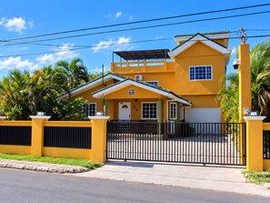 Una casa amarilla de dos pisos con entrada protegida por una reja, un porche cubierto y un garaje.