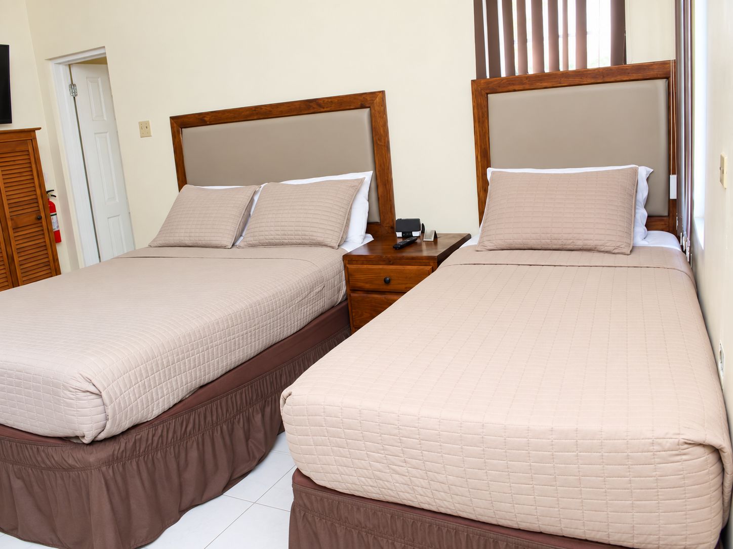 Een hotelkamer met twee bedden, elk met een houten hoofdbord, een nachtkastje en een bedtafel.