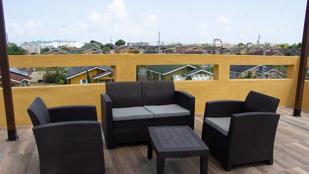A balcony with wicker furniture, a yellow wall, and a view of residential buildings. - The Vista Inn Studio #3 (Falmouth)