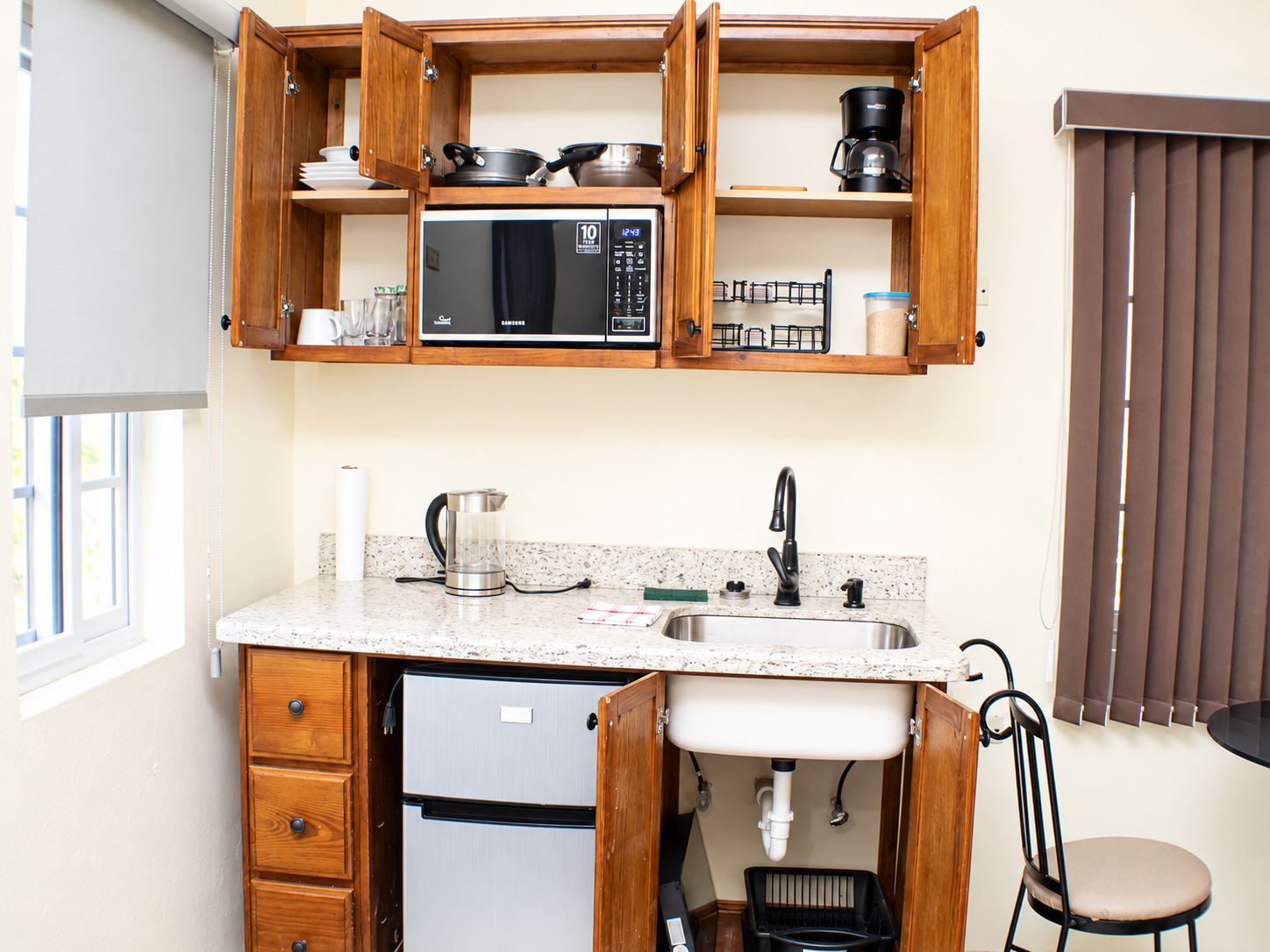 A compact kitchen with a built-in microwave, a stainless steel sink, and wooden cabinetry.