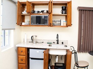 A compact kitchen with a built-in microwave, a stainless steel sink, and wooden cabinetry. - The Vista Inn Studio #3 (Falmouth)