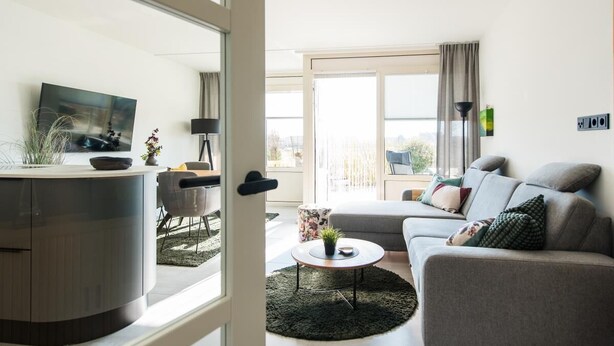 Una sala de estar moderna con un sofá, una mesa de centro, un televisor y un comedor con sillas.