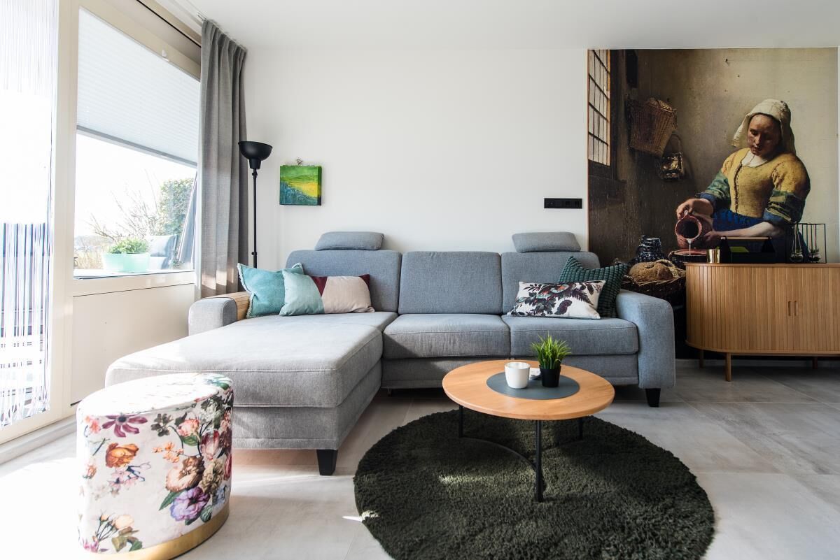 A modern living room with a grey sofa, a round wooden coffee table, a black rug, and a painting of a woman.