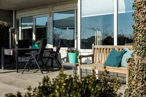 An outdoor patio with a table and chairs, a wooden bench with cushions, and potted plants. - Fräulein Frieda 7 Ameland - great first floor apartment facing south - pets welcome (Ameland)