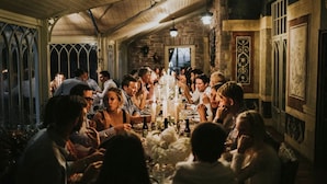 A group of people dining in a room with a wooden ceiling, stone walls, and a large window.
