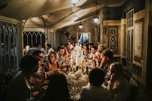 A group of people dining in a room with a wooden ceiling, stone walls, and a large window.