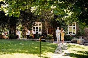 Un bâtiment en pierre avec un chemin pavé menant à une porte, le tout entouré de verdure.