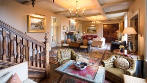 A spacious living room with a grand staircase, a fireplace, and a chandelier.