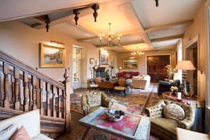 A spacious living room with a grand staircase, a fireplace, and a chandelier.
