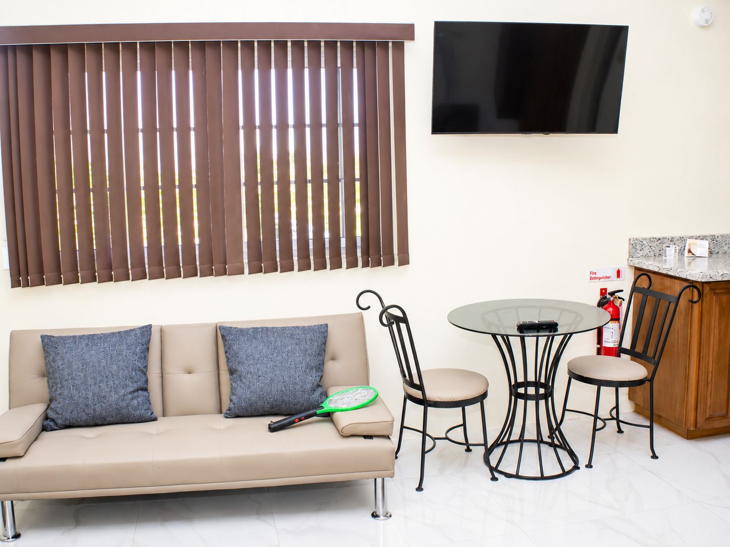 A living room with a sofa, two chairs, a small table, a television, and a fire extinguisher.