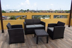 A balcony with wicker furniture, a yellow wall, and a view of residential buildings. - The Vista Inn Studio #4 (Falmouth)