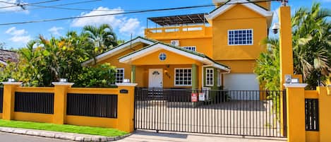 Uma casa amarela de dois andares com portão fechado, garagem e um pequeno alpendre.
