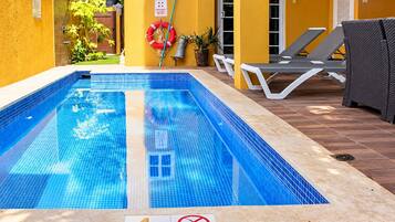 A swimming pool with a 4 ft depth marker, surrounded by lounge chairs and a yellow wall.