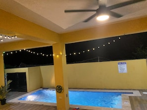 Zona de piscina amb dues piscines, llums penjants, un ventilador de sostre i un cartell amb les normes de la piscina.