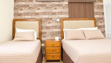 A hotel room with two beds, a wooden wall, a nightstand, and a window with blinds.