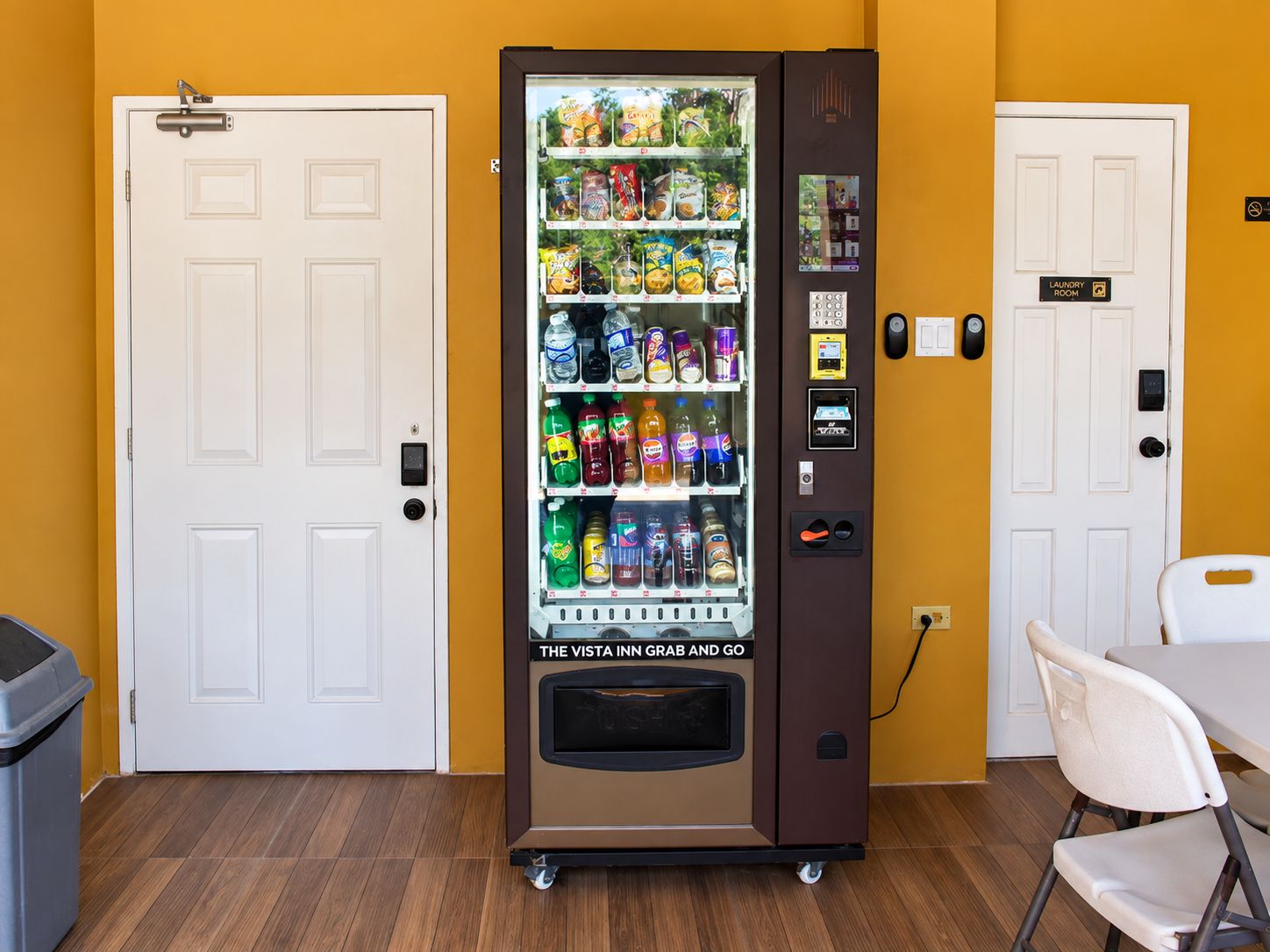 A vending machine with snacks and drinks, a trash bin, and a table with chairs.