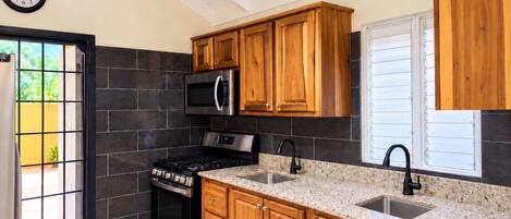 Una cocina con armarios de madera, un microondas de acero inoxidable, una estufa a gas y un grifo negro.