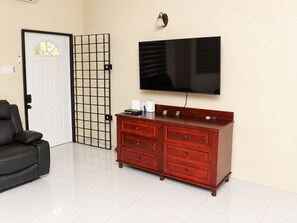 Ein Zimmer mit geschlossener Tür, einem schwarzen Sofa, einem roten Holzschrank, einem flachbildfernseher an der Wand und einer Wandleuchte.