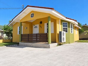 A yellow building with a brown roof, a white door, and a number '322' on the wall.
