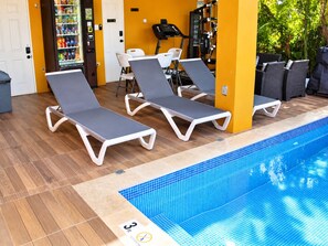 Ein Poolbereich mit Liegestühlen, einem Automaten und Trainingsgeräten.