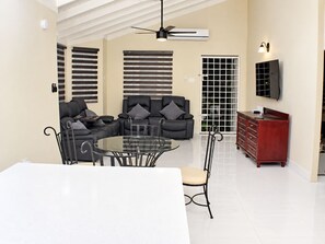A modern living room with a glass dining table, black leather sofas, and a wooden cabinet.