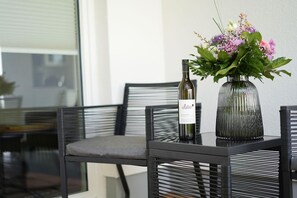 Ein Tisch mit einer Flasche und einer Blumenvase, ein Stuhl und ein Fenster mit Jalousien.