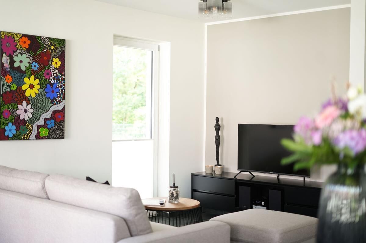 Una sala de estar moderna con un sofá, un televisor, un cuadro y un jarrón con flores.