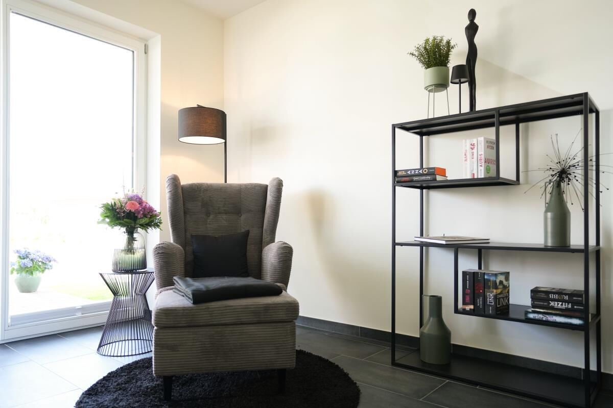 Una sala de estar moderna con un sillón gris, una lámpara de pie negra, una estantería negra y un ventanal con vistas.