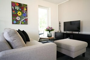 Ein modernes Wohnzimmer mit einer Couch, Hocker, Fernseher und Kunstwerken.