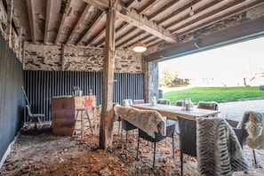 An outdoor dining area with rustic wooden beams, a stone wall, and a view of a grassy field. - Vogel House - Six Bedroom Villa, Sleeps 14 (Llangynhafal)