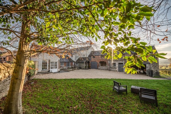 A traditional stone building with a gravel courtyard, a grassy lawn, and a bench.