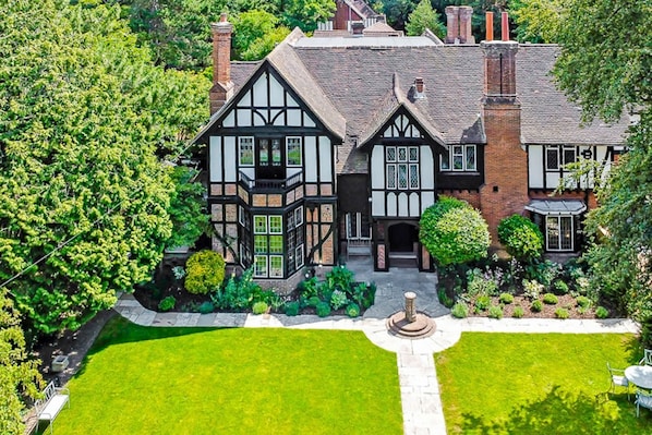 A Tudor-style house with a symmetrical facade, a central entrance, and a well-manicured garden with a fountain.