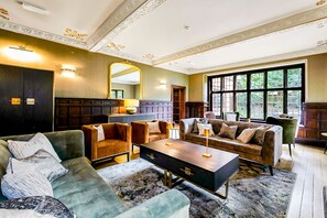 A spacious living room with a large window, a fireplace, and a high ceiling with decorative moldings.