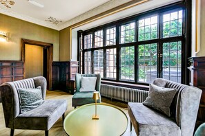 A room with two armchairs, a round table, and a large window with a view of greenery.