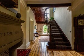 Eine prachtvolle Treppe führt zu einer zweiten Etage, ein Kamin mit einer Plakette und eine Uhr an der Wand.