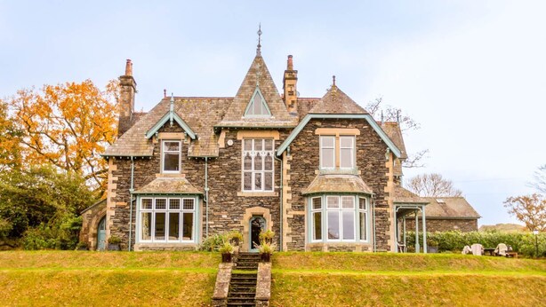 A stone house with a steeply pitched roof, multiple chimneys, and a prominent turret window. - Lakestone House - Five Bedroom Villa, Sleeps 10 (Windermere)