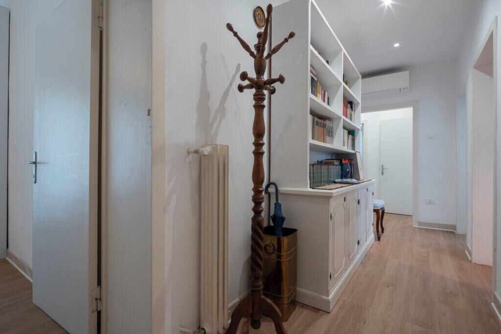 Un couloir avec un porte-manteau, un radiateur, une bibliothèque et une porte.