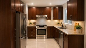 A modern kitchen with dark wooden cabinets, stainless steel appliances, and a tiled floor. - Luxury apartment 3BR (Longueuil)